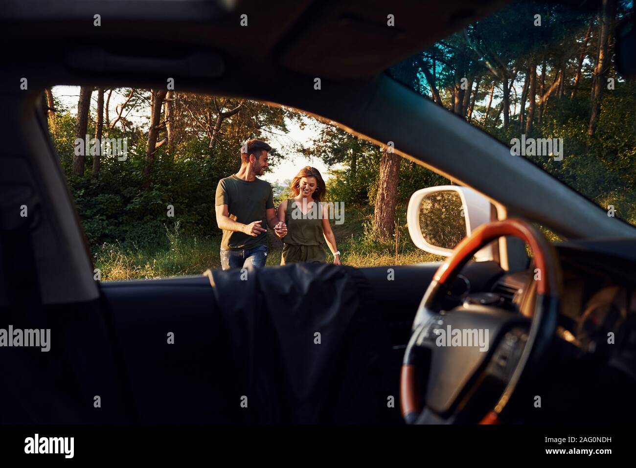 Blick vom Inneren des Autos. Lenkrad, Außenspiegel. Schöne junge Paare haben eine gute Zeit im Wald bei Tag Stockfoto