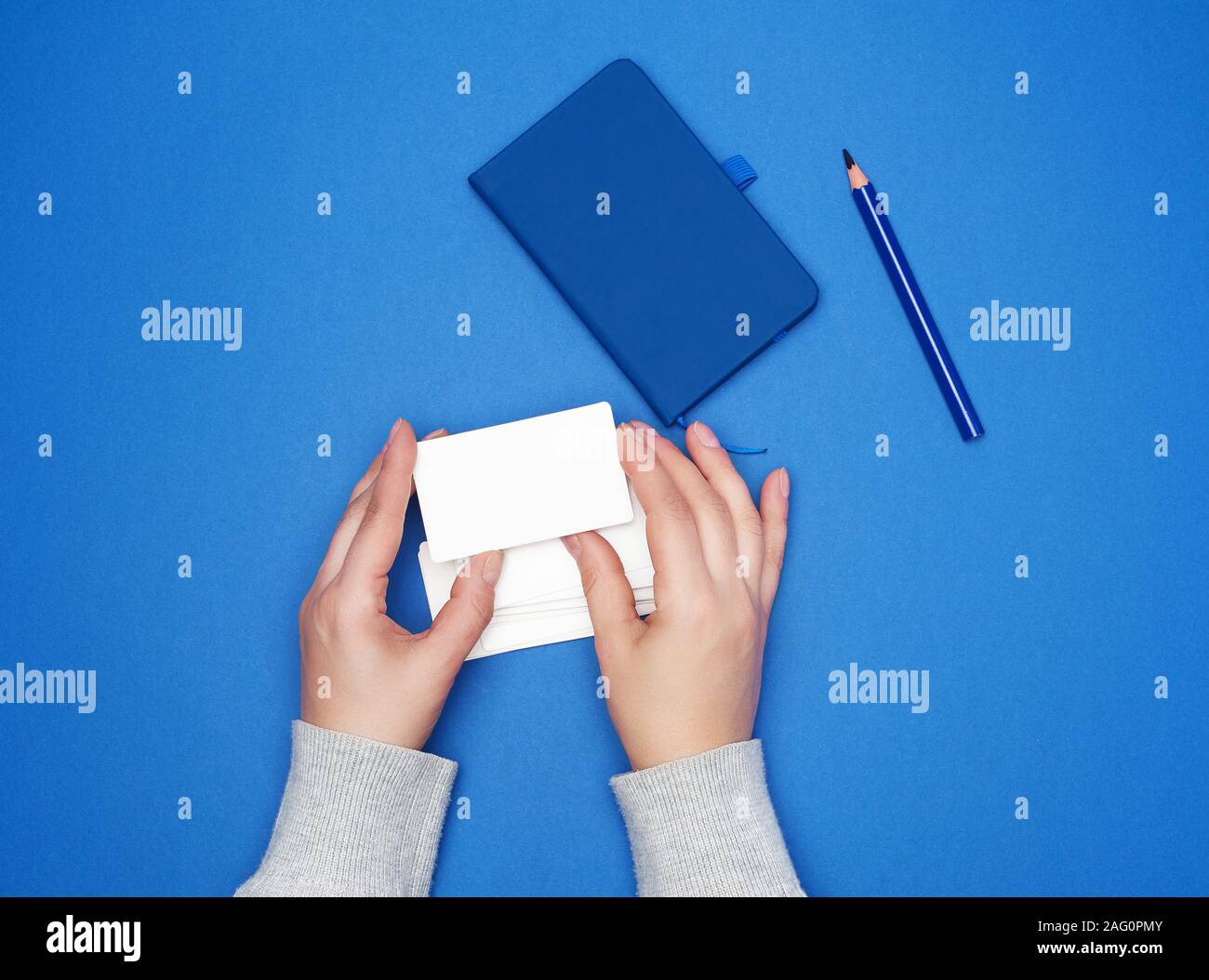 Zwei weibliche Hände halten eine leere weiße Visitenkarten auf einem blauen Hintergrund, Top View Stack Stockfoto