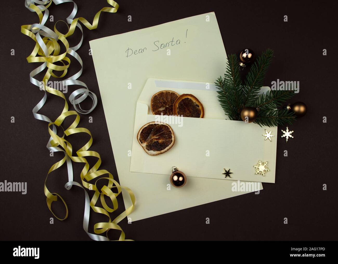 Liebes Christkind Brief geschrieben für Weihnachten. Papier und Umschlag mit Zweig der Fichte und getrockneten Schicht von Orange auf braune Oberfläche. Stockfoto