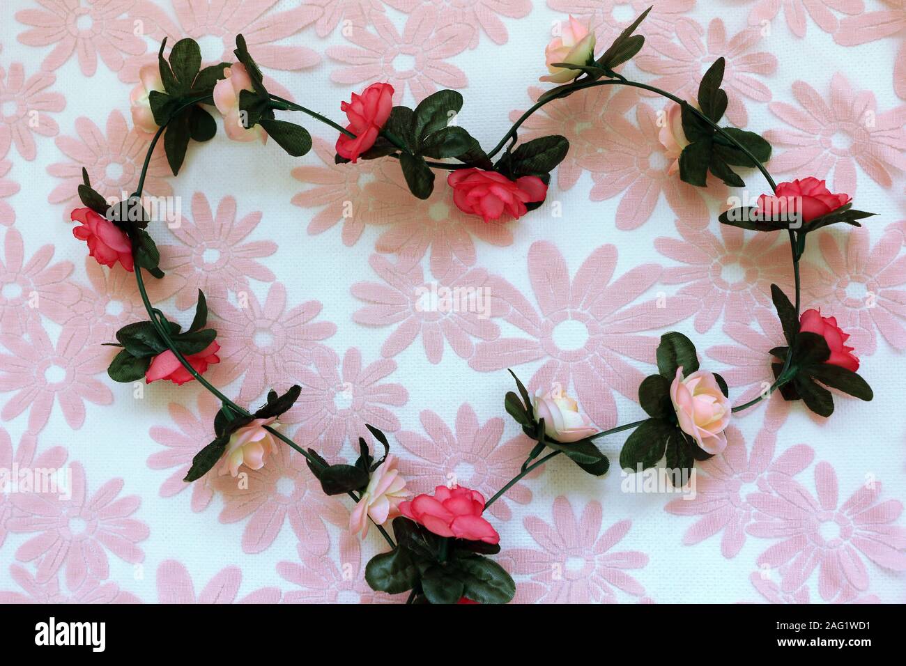 Eine Zeichenkette von Stoff Rosen in der Form eines Herzens auf eine rosa Blume Hintergrund Stockfoto