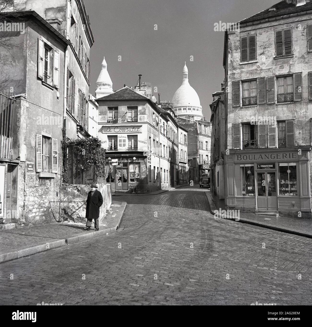 1950er Jahre, historisch, Blick auf das Le Consulat Restaurant, 18 Rue Norvins, Paris, Frankreich, ein historisches Café auf einer Kopfsteinpflasterstraße im Zentrum von Montmartre, dem künstlerischen Viertel der Stadt. Die berühmten Kuppeln der Kathedrale Notre Dame sind in der Ferne zu sehen. Stockfoto