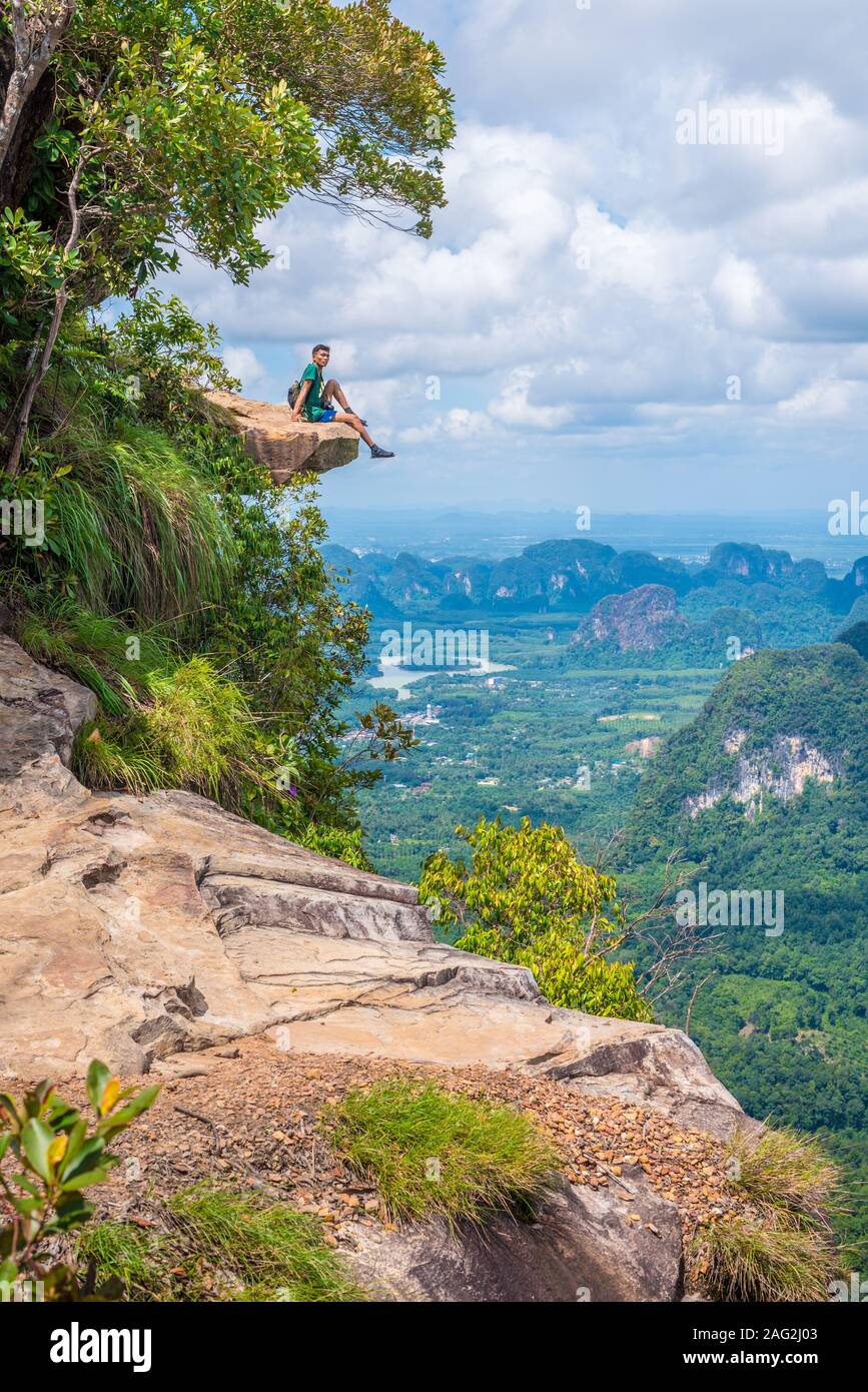 Junger Mann sitzt auf Felsen, ragt über den Abgrund, mit schönen Landschaft. Dragon Crest in Khao Ngon Nak Naturlehrpfad in Krabi. Stockfoto