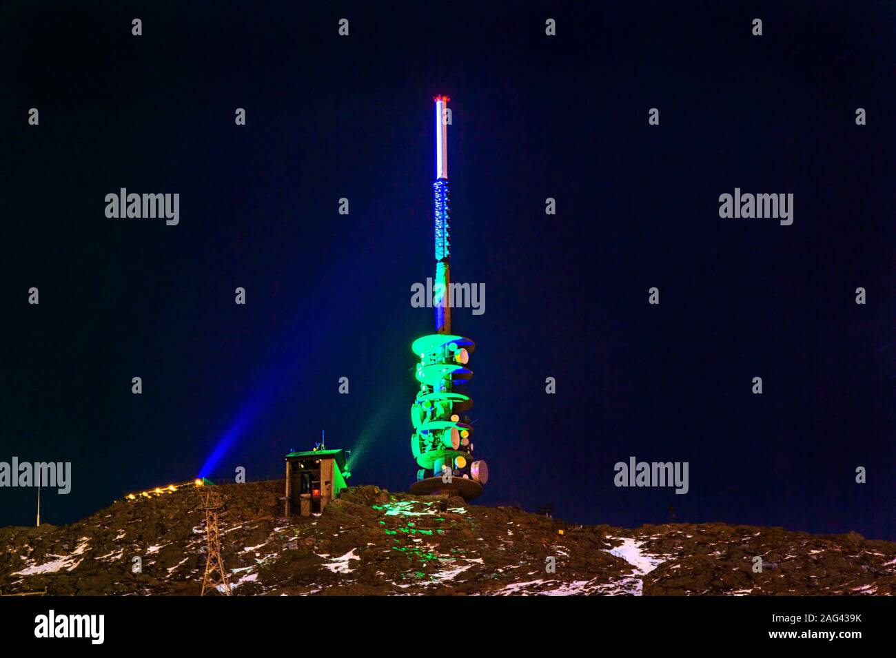 TV-Antenne Tower auf der Spitze eines Berges durch farbiges Licht in der Nacht beleuchtet. Stockfoto