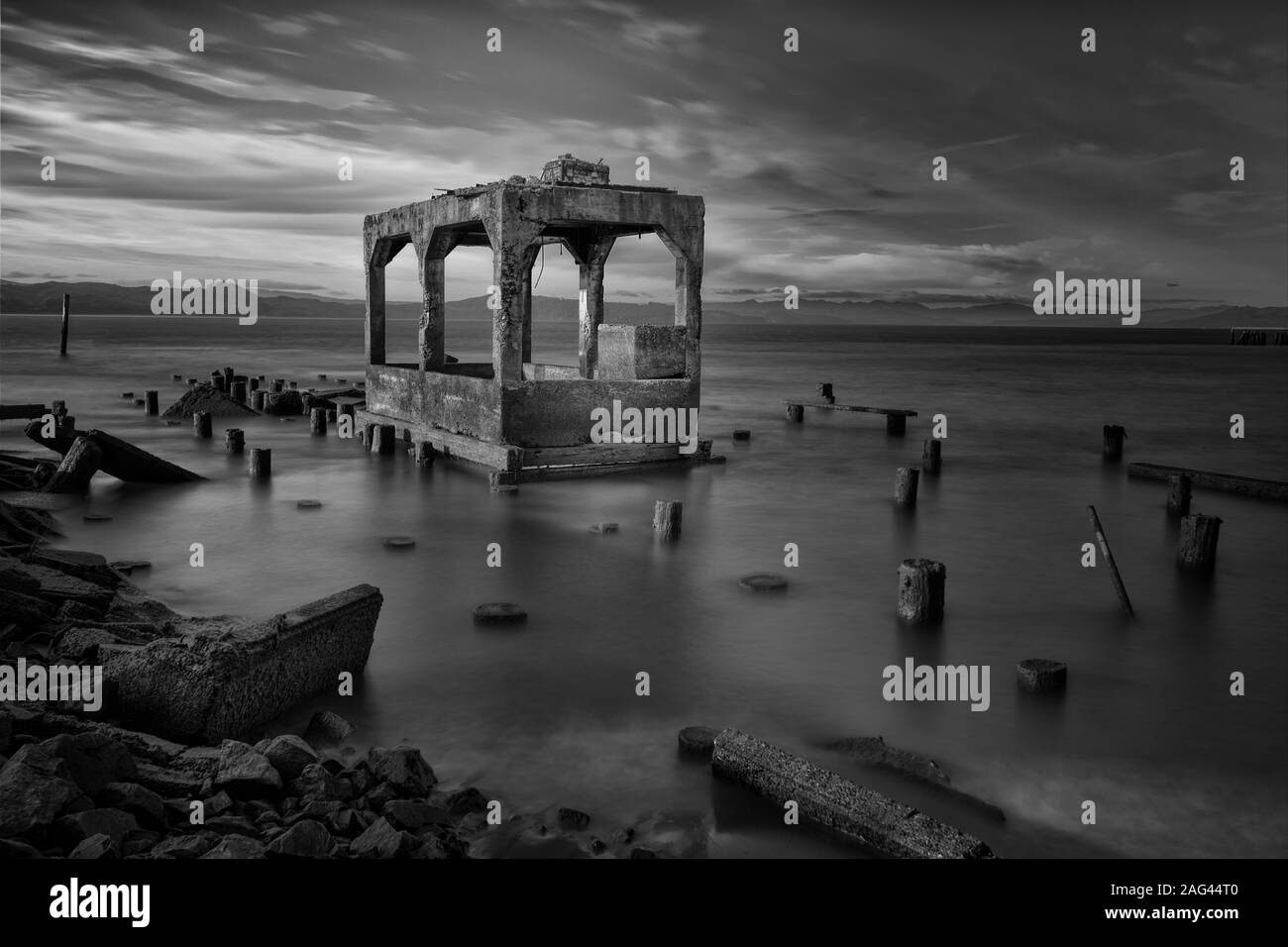 Graustufen Aufnahme der Gebäude Ruinen von Holzstämmen umgeben in Das Meer unter dem schönen bewölkten Himmel Stockfoto