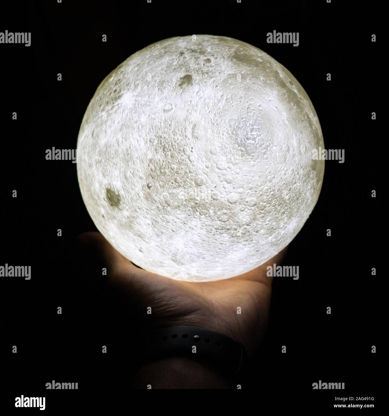 Nahaufnahme einer weiß beleuchteten Planetenfigur in einem Menschliche Handfläche auf schwarzem Hintergrund Stockfoto
