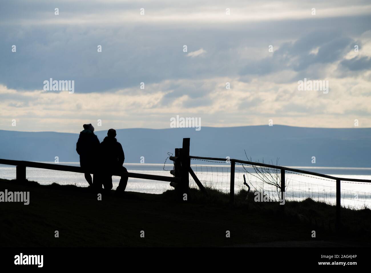 Aufnahme von Silhouetten von Menschen bewundern die Schönheit der Meer unter dem wolkigen Himmel Stockfoto