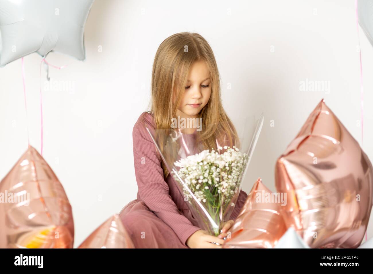 Sieben Jahre alten Mädchen sitzt auf einem weißen Hintergrund Kleid mit einem Blumenstrauß aus den weißen Wildblumen und Ballons Stockfoto