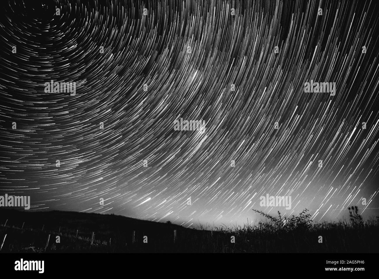Graustufen Aufnahme der atemberaubenden Spirallichter in der Nachthimmel über einem Hügel Stockfoto