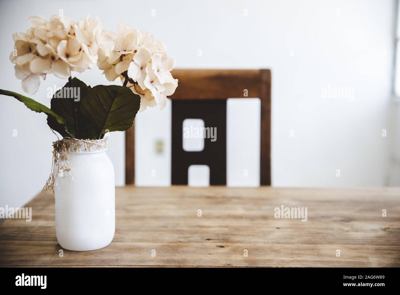 Nahaufnahme von weißen Blumen in einem weißen Glas auf Ein Holztisch mit unscharfem Hintergrund Stockfoto