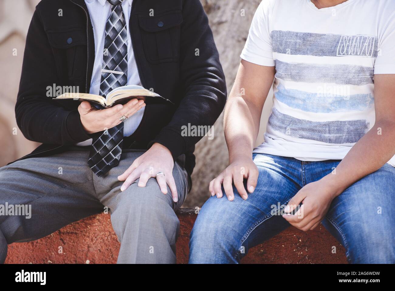 Nahaufnahme von zwei Männern sitzen, während einer von ihnen Liest die bibel mit verschwommenem Hintergrund Stockfoto