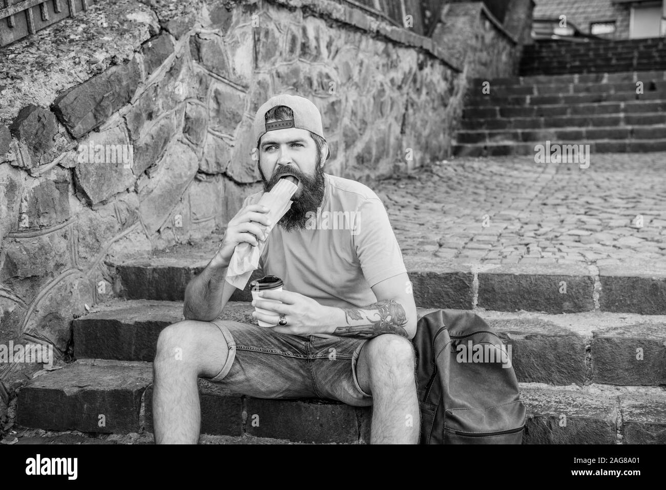 Mahlzeit einfach besser schmeckt. Hipster essen Hot Dog Essen auf Treppen im Freien. Kaukasische Kerl genießen essen Essen zum Mitnehmen. Bärtiger Mann isst ungesund hotdog Sandwich während der Ruhe- und Essenspause. Stockfoto