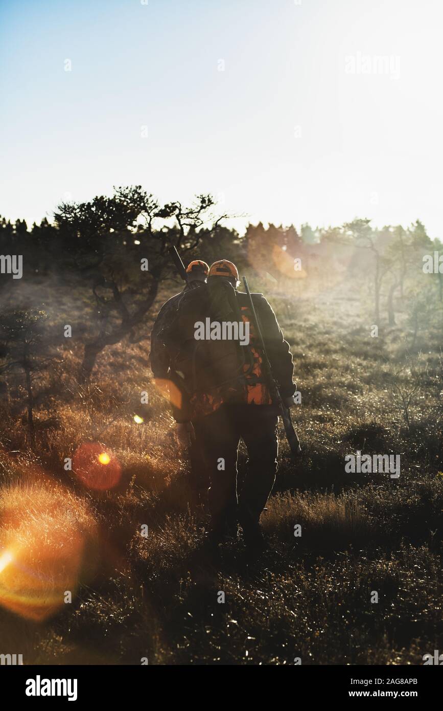 Vertikale Aufnahme von zwei männlichen Jägern mit Gewehren, die hereinlaufen Der Wald unter dem Sonnenlicht Stockfoto
