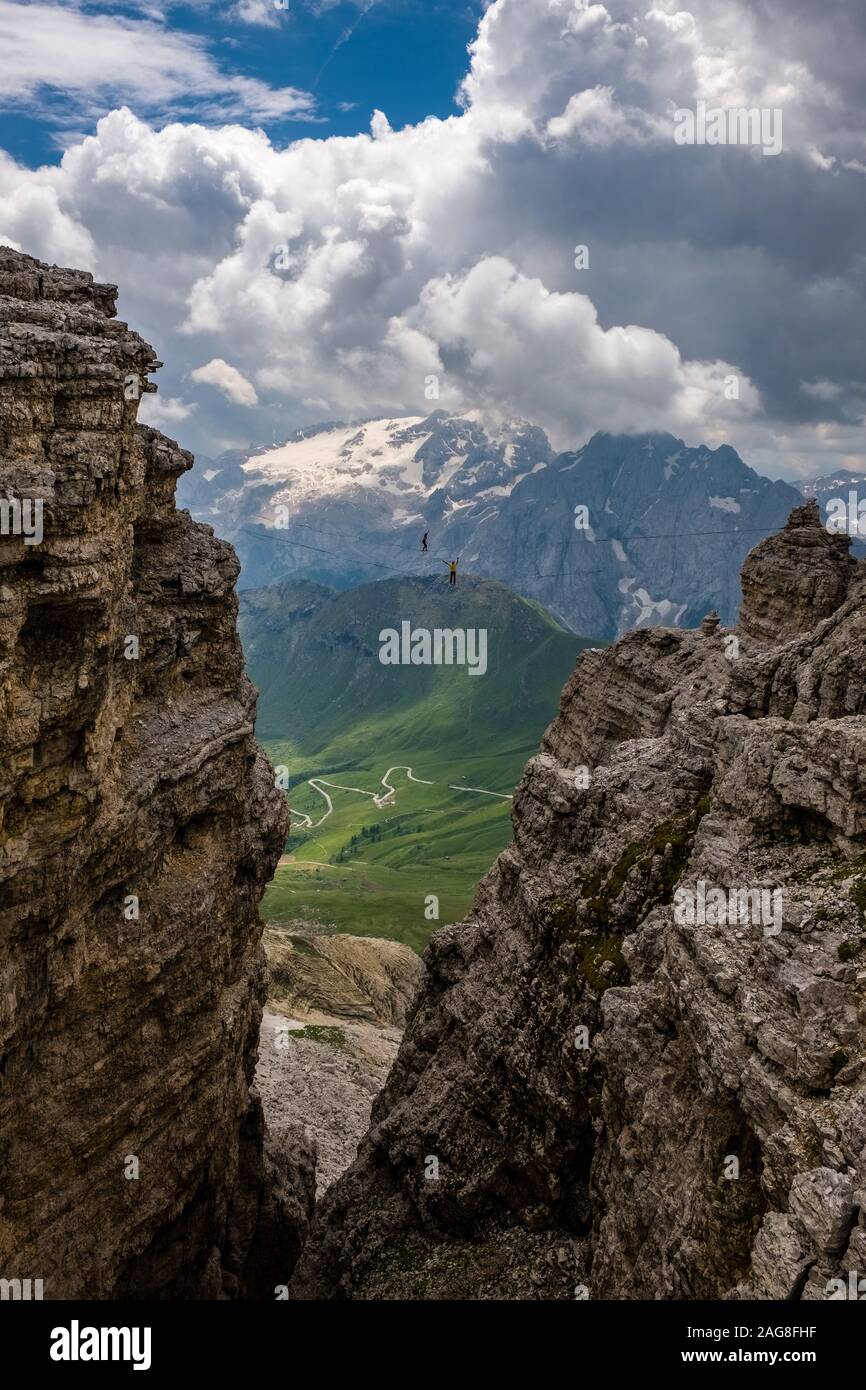 Zwei Personen sind zu Fuß auf der slackline zwischen den Felsen des Plateaus Sass Pordoi, die schneebedeckten Marmolata, Marmolada Gletscher und Gipfel in den distan Stockfoto