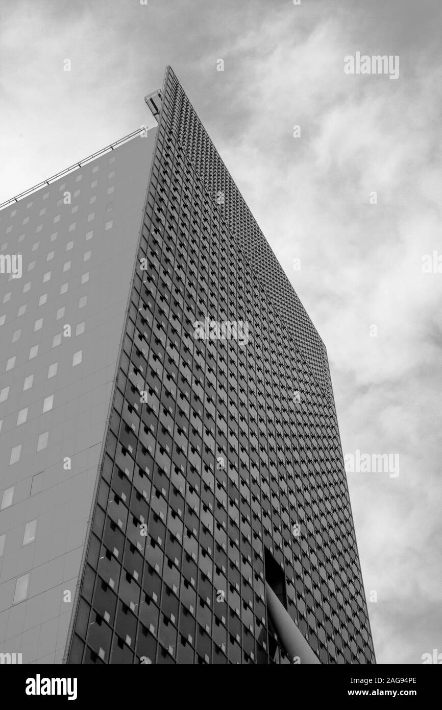 Vertikale Graustufenaufnahme eines Hochhauses unter einem niedrigen Winkel Der bewölkte Himmel Stockfoto