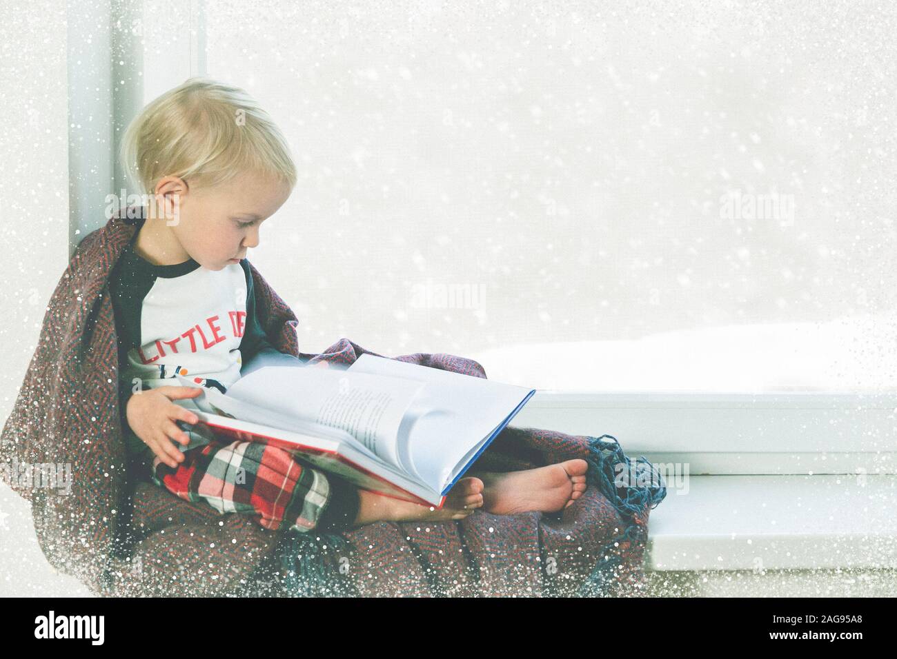 Kind liest Buch durch das Fenster. Schönes Winterwetter mit Schnee Stockfoto