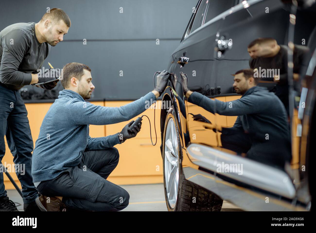 Zwei Auto service Arbeitnehmer Prüfung Karosserie auf Kratzer und Schäden, während Sie ein Auto für Professional automotive Details Stockfoto