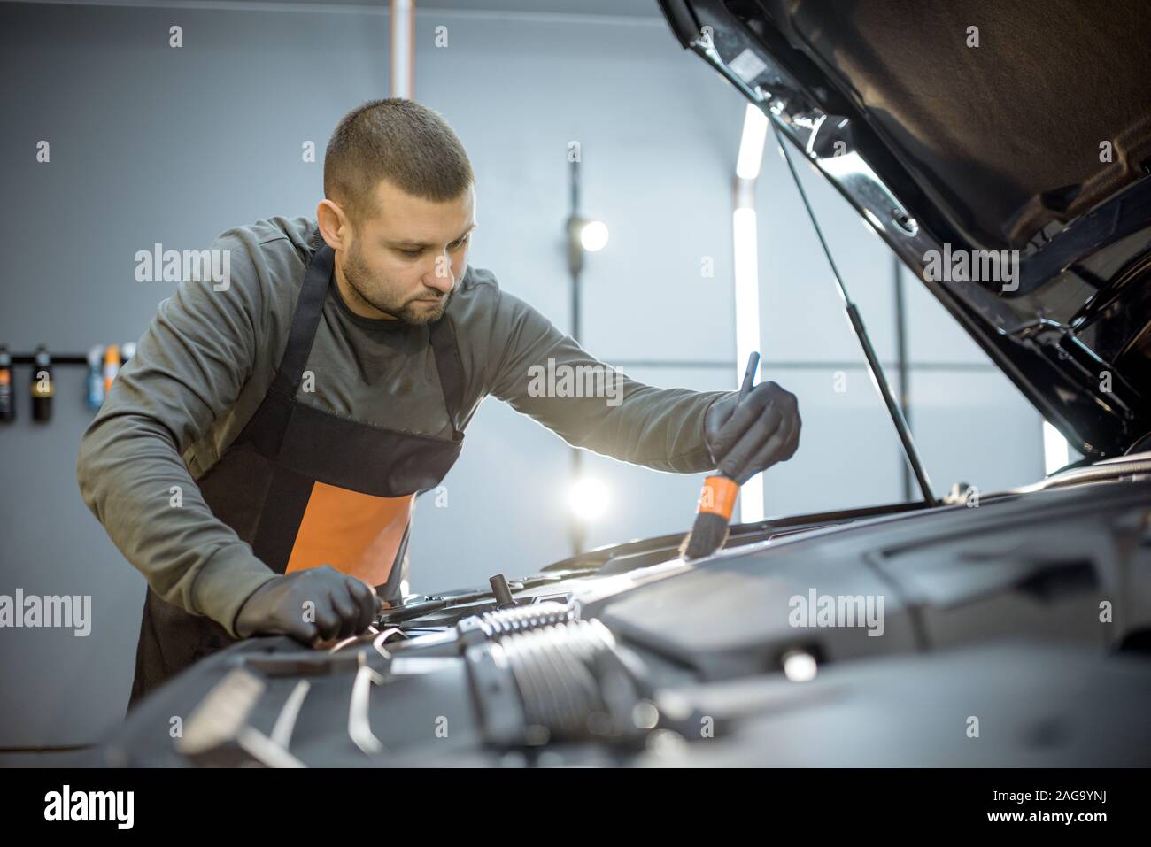 Mann führt eine professionelle Reinigung, Waschen Motor mit Pinsel und Waschmittel in der Service-station Stockfoto
