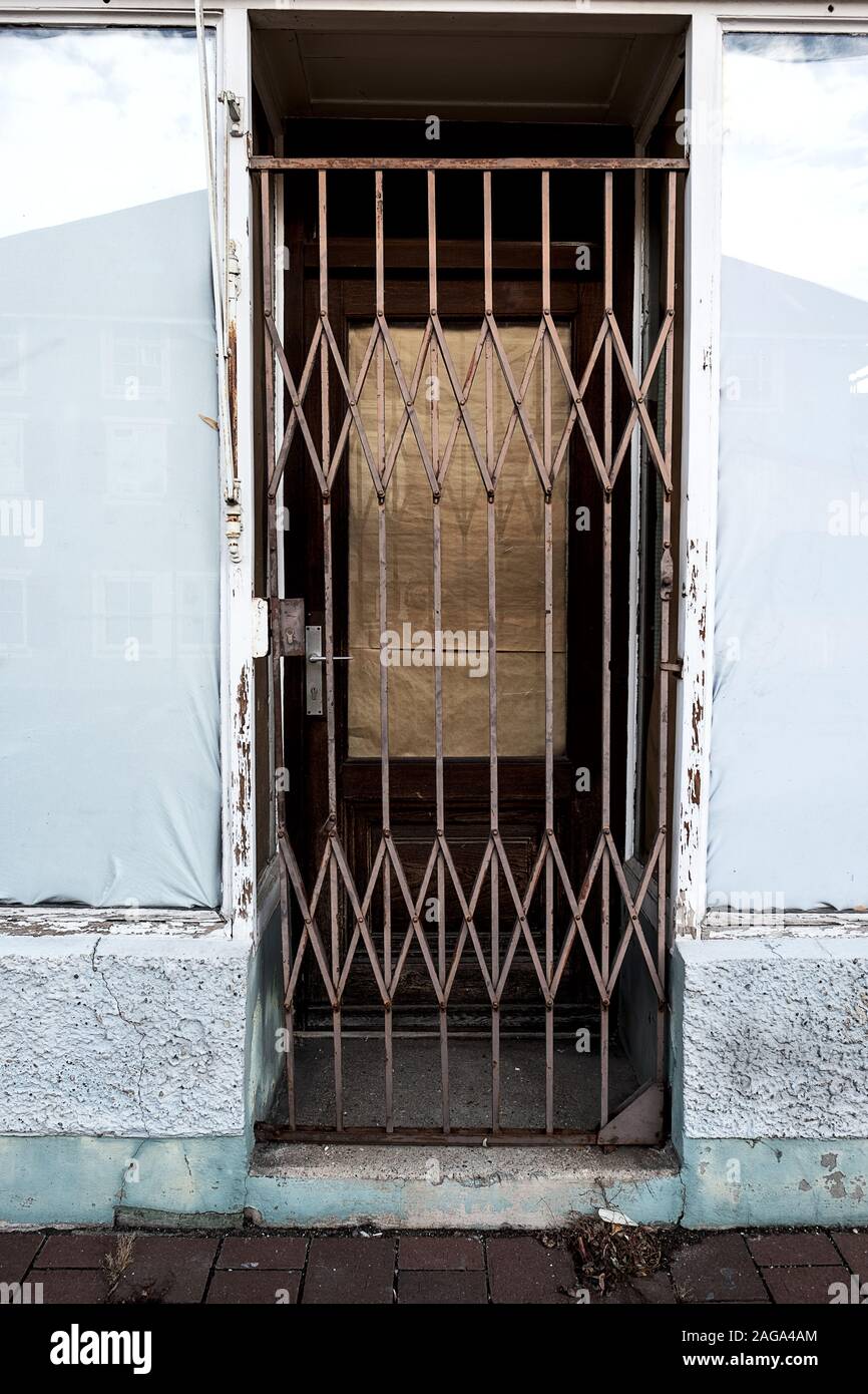 Tür eines verlassenen Shop gesichert mit einem Stahlgitter, die Fenster mit Papier und Folie abgedichtet Stockfoto