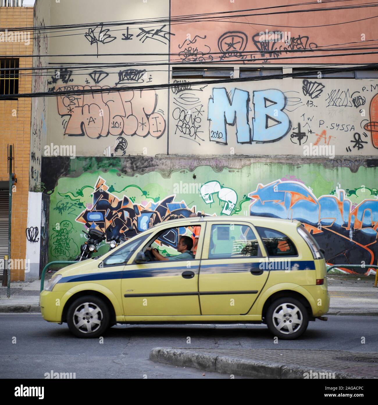 Brasilianische Taxi. Ein Taxi vorbei an einem stark entstellt Wand in Graffiti tags in den Straßen von Rio de Janeiro. Stockfoto