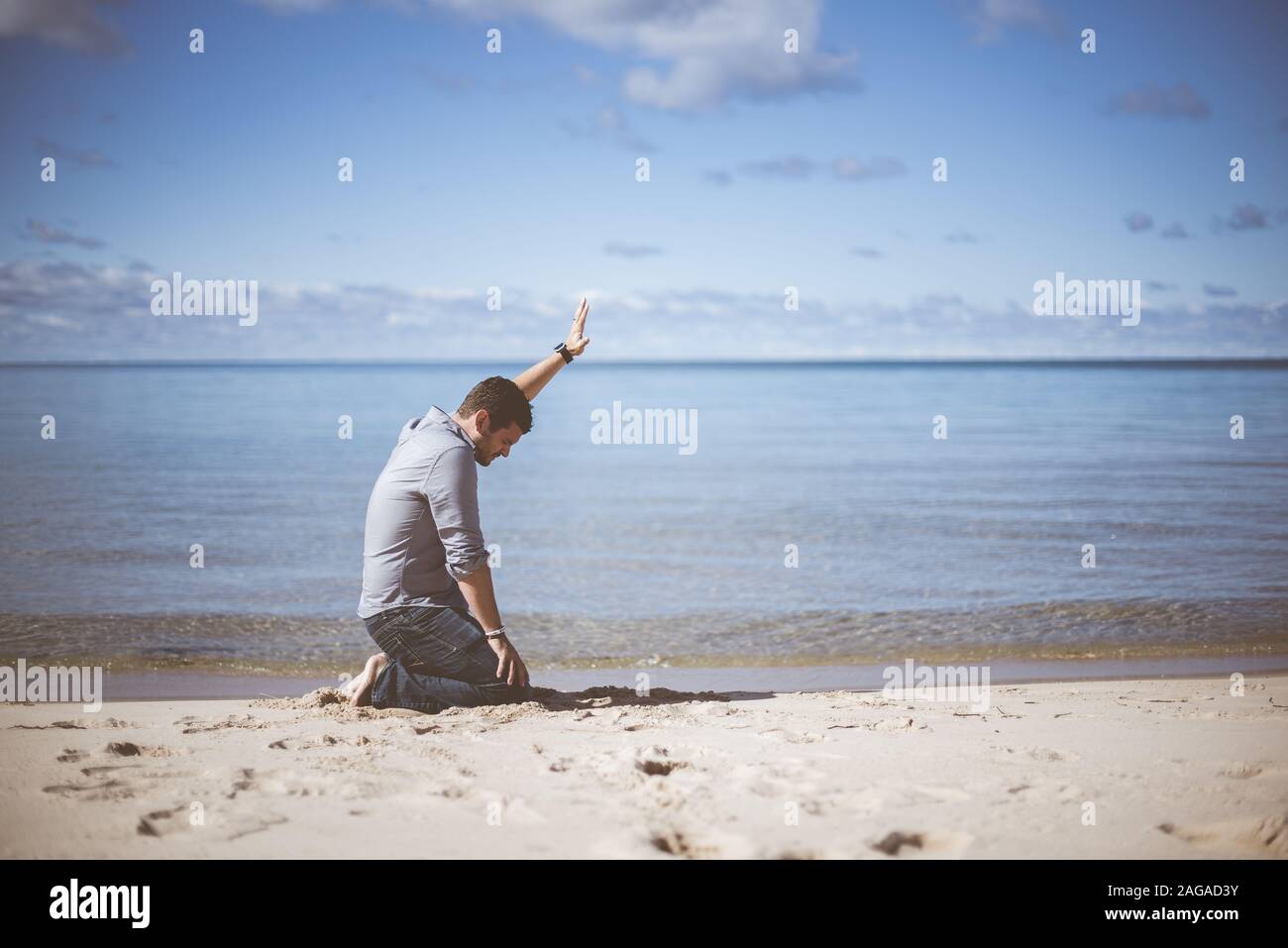 Männlich auf den Knien auf einer sandigen Oberfläche mit Seine Hand beim Beten hoch Stockfoto