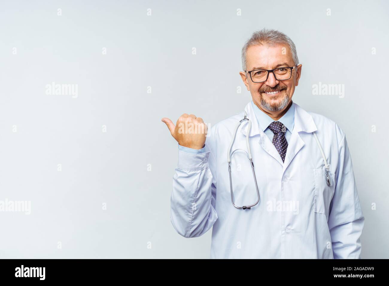 Fröhliche reife Arzt posing und lächelnd an Kamera, Gesundheitswesen und Medizin. Auf blauem Hintergrund isolieren. Hand bei copy Raum zeigt. Stockfoto