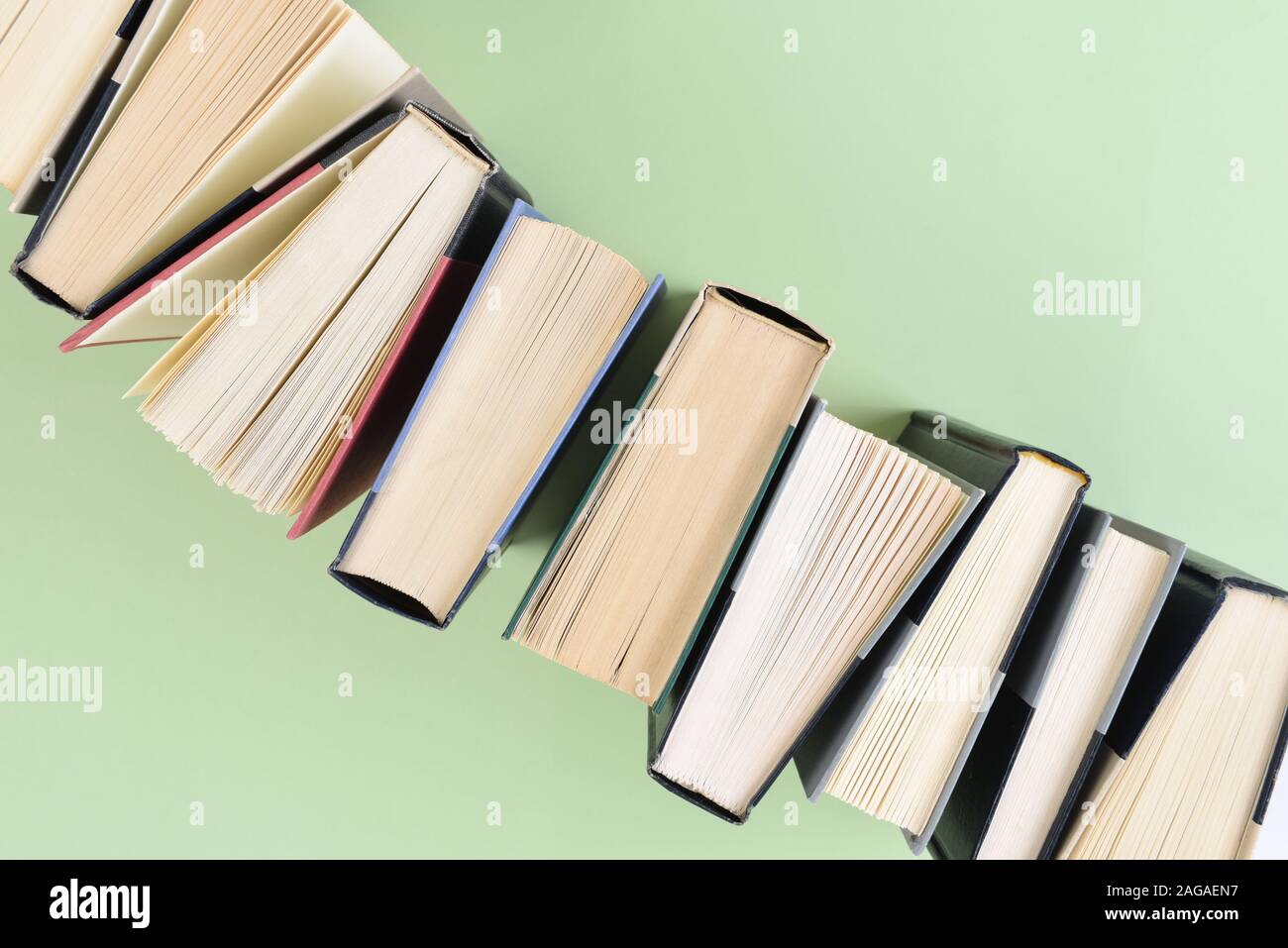 Eine Linie der Bücher stehen auf Ende in einem Winkel bilden eine Ecke des Rahmens in die entgegengesetzte Ecke läuft, auf einem hellgrünen Hintergrund. Stockfoto