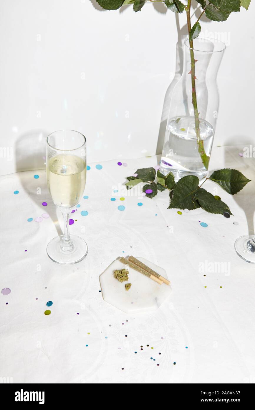 Vertikale Aufnahme von Gläsern Champagner, Marihuana Blunts und einer weißen Rose auf weißem Hintergrund Stockfoto