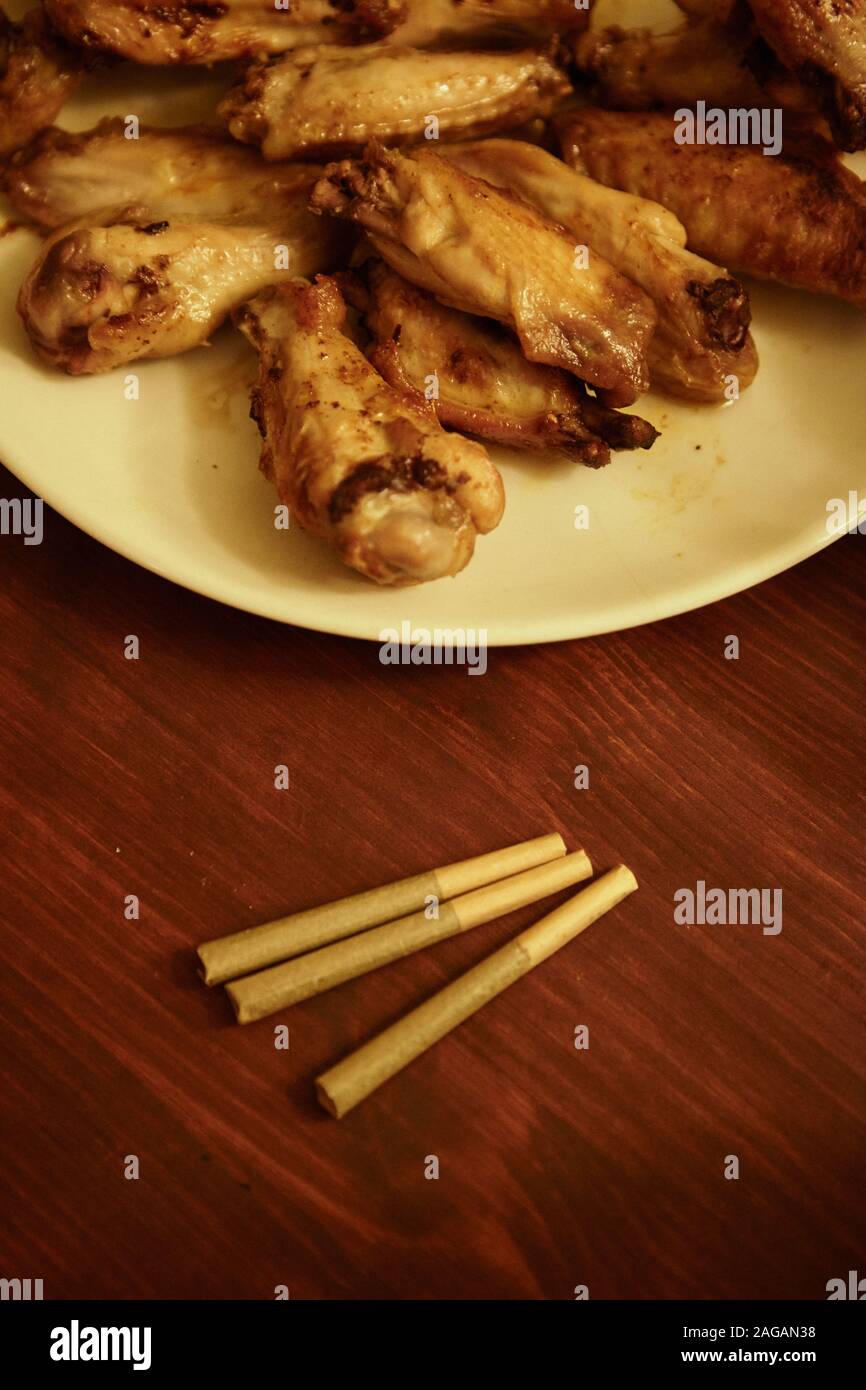Vertikale Aufnahme von Marihuana Blunts auf einem Holztisch mit Ein Teller gebratenes Huhn Stockfoto