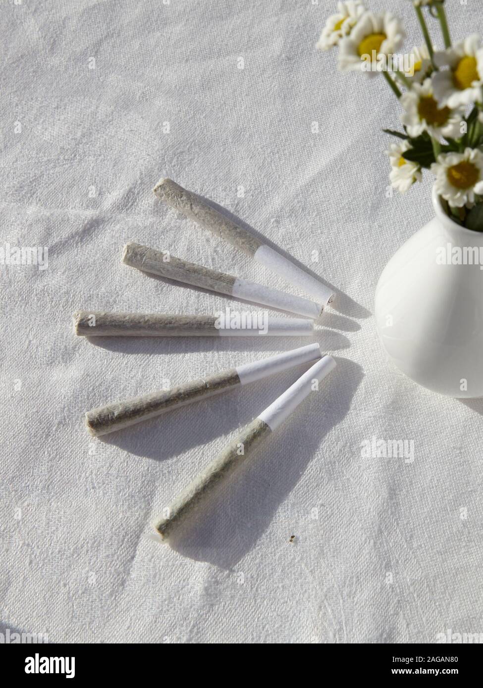 Vertikale High-Angle-Aufnahme von Marihuana-Blunts und einer Vase Von Kamillen auf einer weißen Oberfläche Stockfoto