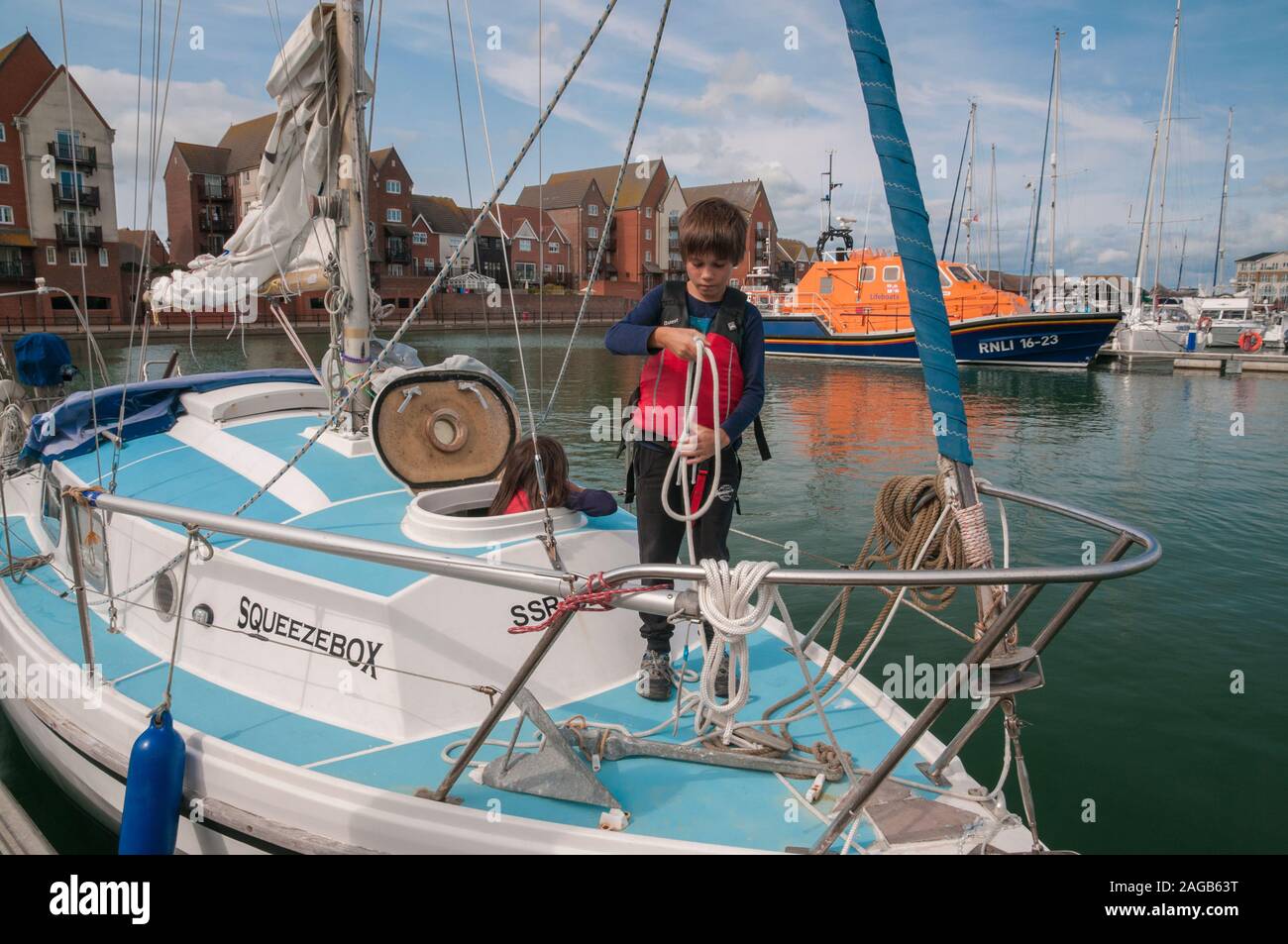 Junge das Tragen einer Schwimmweste stehen auf einer Yacht, wickeln Seil, Sovereign Harbour Marina, East Sussex, Großbritannien Stockfoto