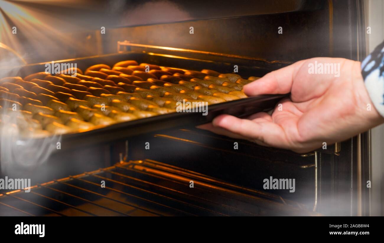 Weibliche hand Backblech mit Vanille Brötchen zu einem offenen Heiß dampfenden Backofen. Gestapelte sichelförmigen raw Süßigkeiten aus Nussigen Teig auf flachem Blatt pan. Stockfoto