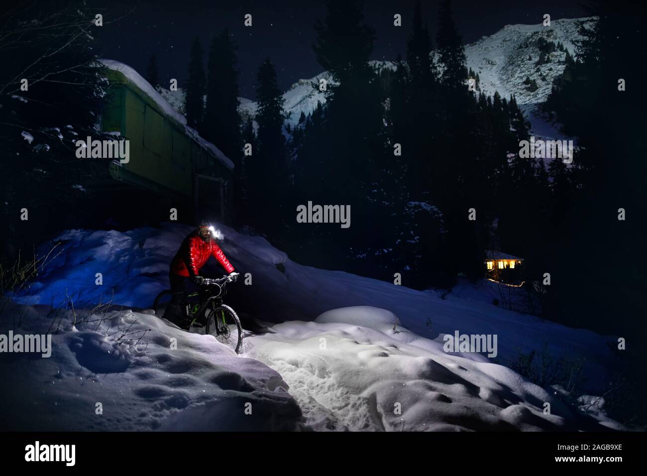 Mann im roten Mantel mit Fahrrad im Winter verschneite Wald in den Bergen unter Nachthimmel mit Sternen Stockfoto