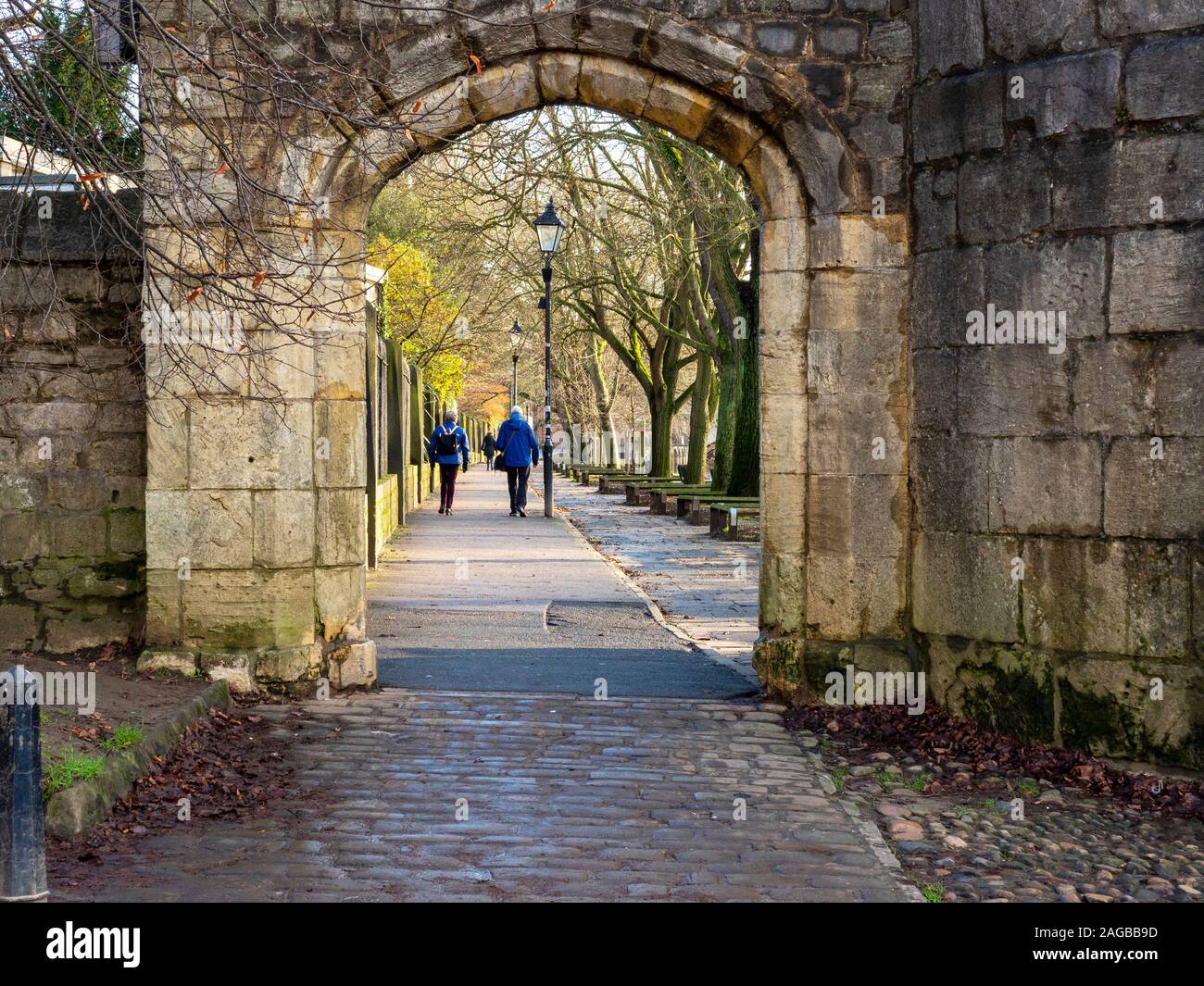 Blick durch einen Steinbogen zu ein paar Flanieren auf den von Bäumen gesäumten Riverside Dame Judi Dench in York, England Stockfoto