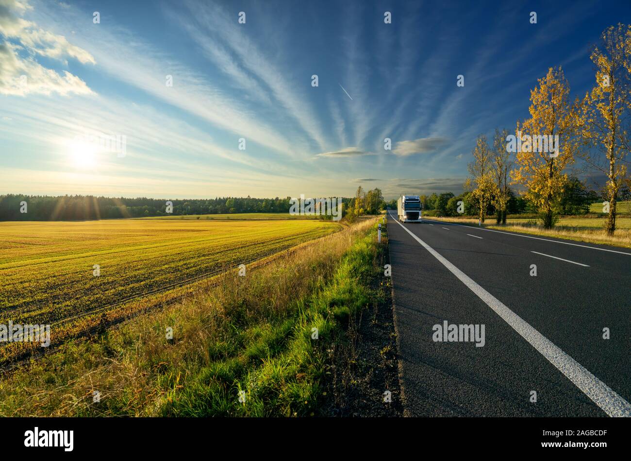 Weiße Fahrzeug anreisen, aus einer Entfernung auf eine asphaltierte Straße im Herbst Landschaft bei Sonnenuntergang Stockfoto