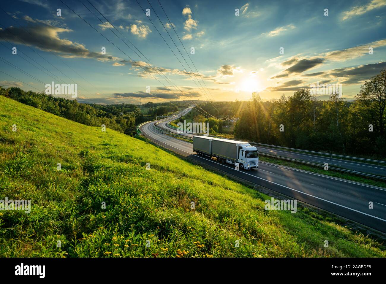 Weiße Lkw fahren auf dem Asphalt Autobahn in Landschaft bei Sonnenuntergang Stockfoto