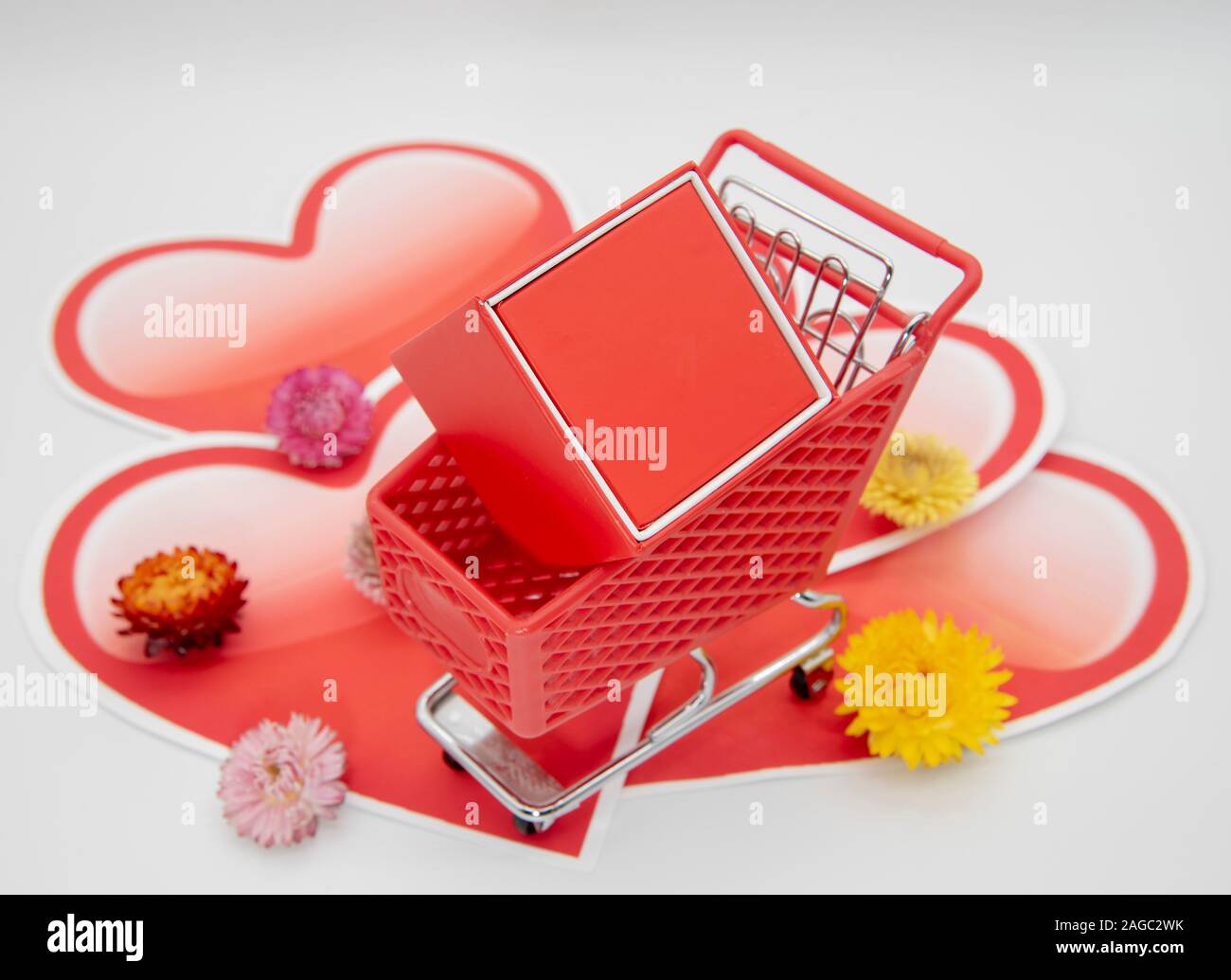 Shopping Cart mit roter Geschenkbox auf einem Hintergrund von Papier Herzen Stockfoto
