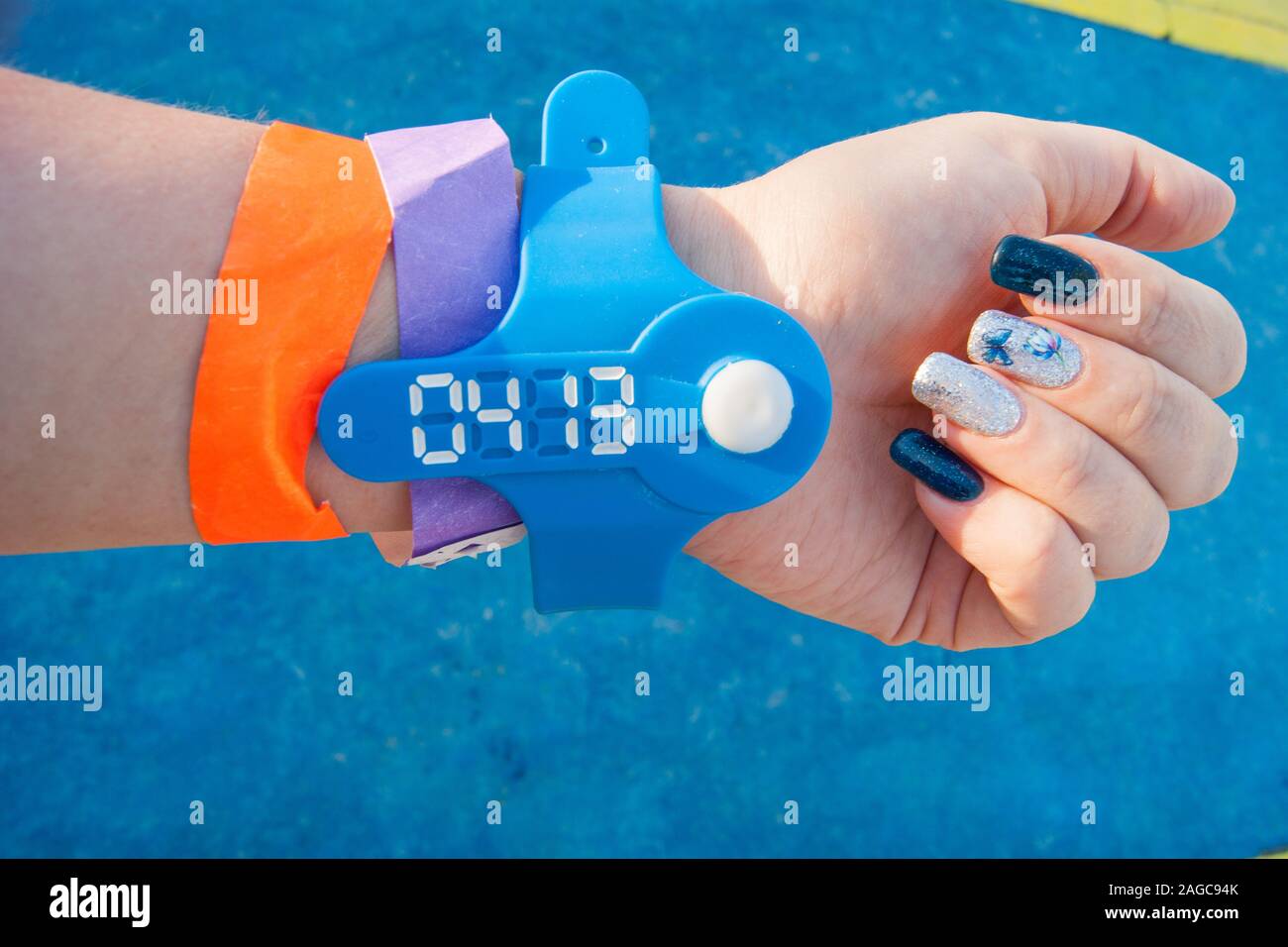 Die Stimmung Farbe blau ist - eine weibliche Hand gegen die blauen Boden in farbigen Armbänder aus dem Wasser park, Nägel sind auch in blau lackiert Stockfoto