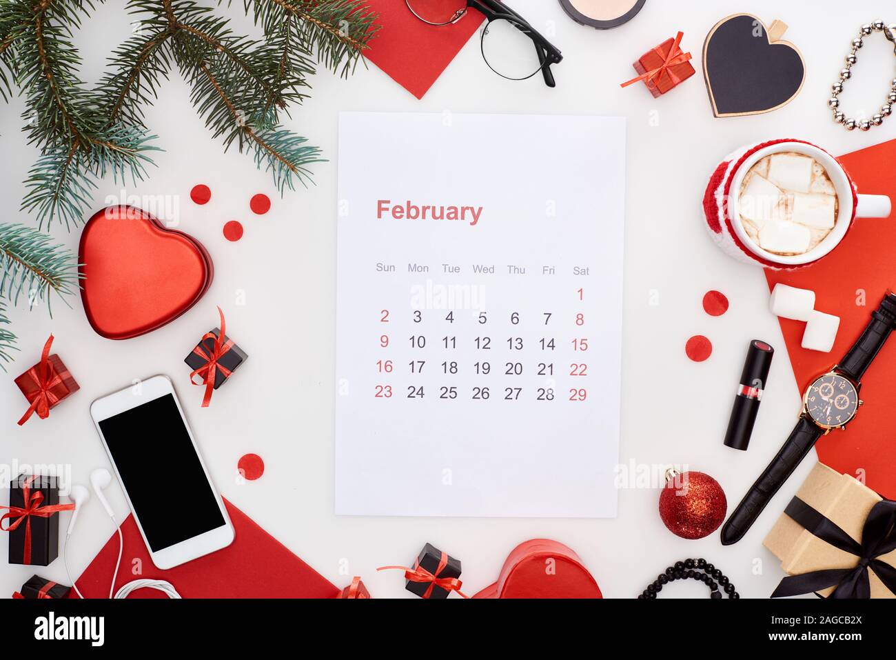 Februar Kalender Seite, Kaffee mit Marshmallow, Smartphone, Tanne, Armbanduhr, Armreifen, Christbaumkugeln, rotes Papier, Armbanduhr auf w isoliert Stockfoto