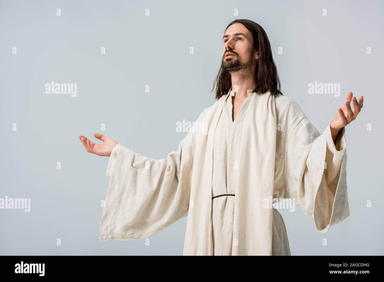 Mann in Jesus Gewand mit ausgestreckten Händen isoliert auf Grau Stockfoto