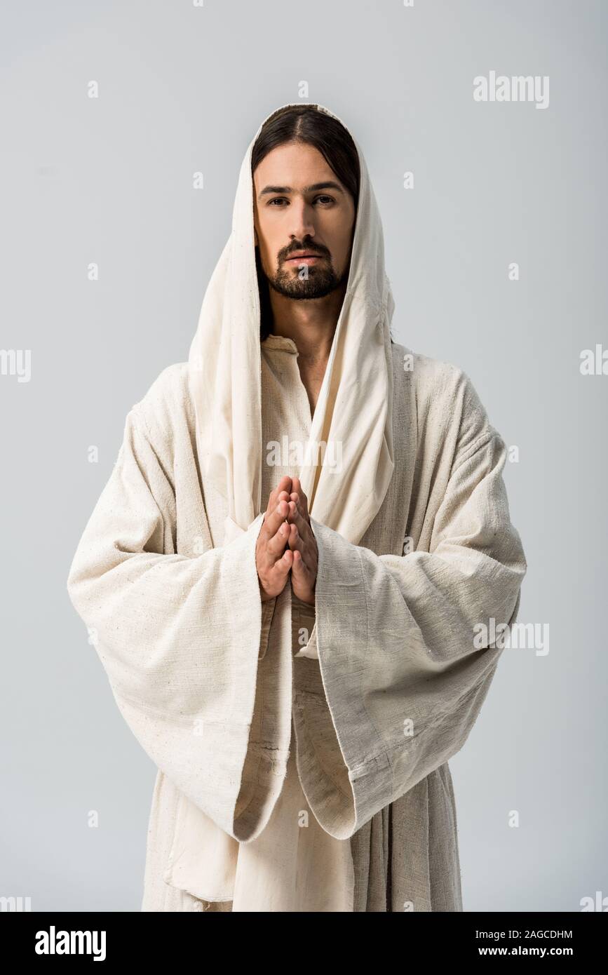 Religiöser Mensch mit betenden Händen und Jesus Gewand mit Haube stehen isoliert auf Grau Stockfoto