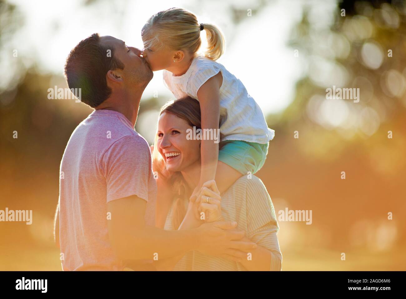 Glückliche junge Mädchen sitzen auf ihrer Mutter Schultern und küsste ihre Vater. Stockfoto