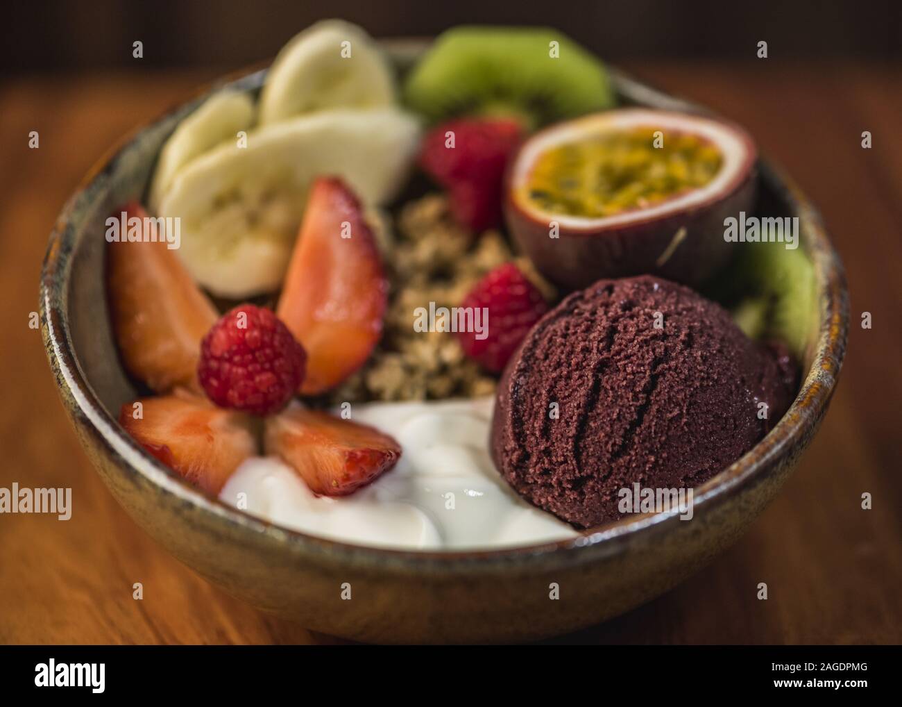 Köstliche Schüssel mit Joghurt, Eis, Nüssen und frischem Obst auf einer Holzoberfläche Stockfoto