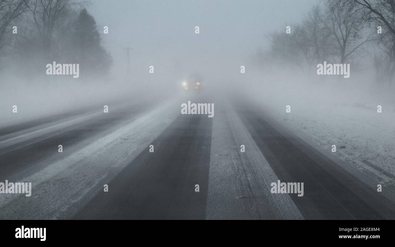 Ein Foto durch die Windschutzscheibe des Autos während eines Winters Sturm genommen (auf der Straße). Die Lichter der entgegenkommenden Autos. Stockfoto