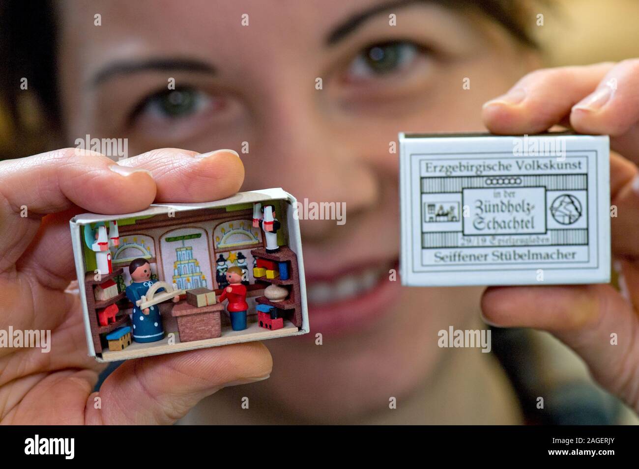 11 Dezember 2019, Sachsen, Seiffen: Cornelia Flath zeigt in der Schauwerkstatt des "eiffner Stübelmacher', ihr Vater Gunter Flath, eine Streichholzschachtel mit der Darstellung eines Toy Shop im Miniaturformat. Mit dem Design und der Herstellung der streichholzschachteln und die so genannte Dübel, der junge Meister Drechsler und Spielzeughersteller weiterhin eine alte Tradition der erzgebirgischen Volkskunst. Neben der Streichholzschachteln, der Werkstatt in erster Linie produziert Miniatur Stuben, die jeweils aus mehr als 100 Einzelteilen in Millimeter Größe. Sie geben Einblicke in das Leben und die Arbeit der früheren Generationen in t Stockfoto