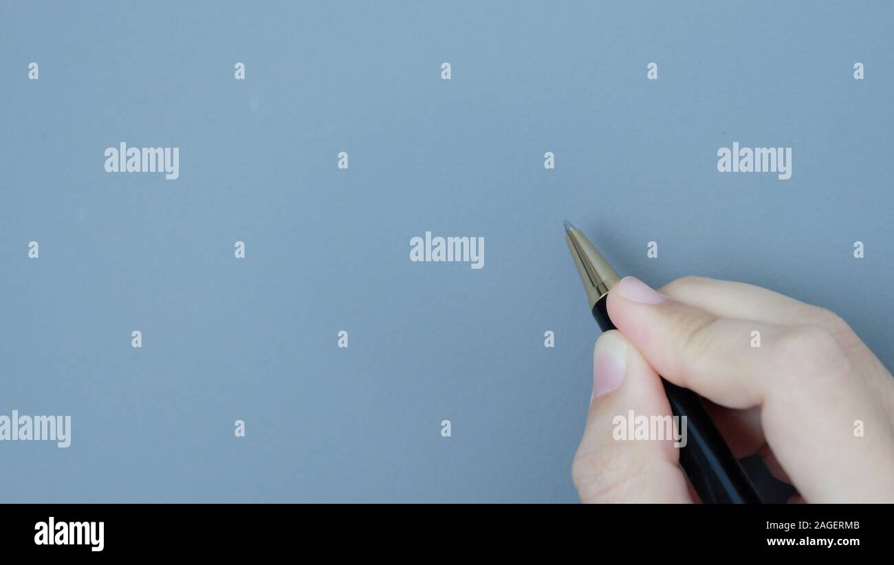 Hand mit einem Kugelschreiber, in der Geste der Schrift auf grauem Hintergrund. Stockfoto