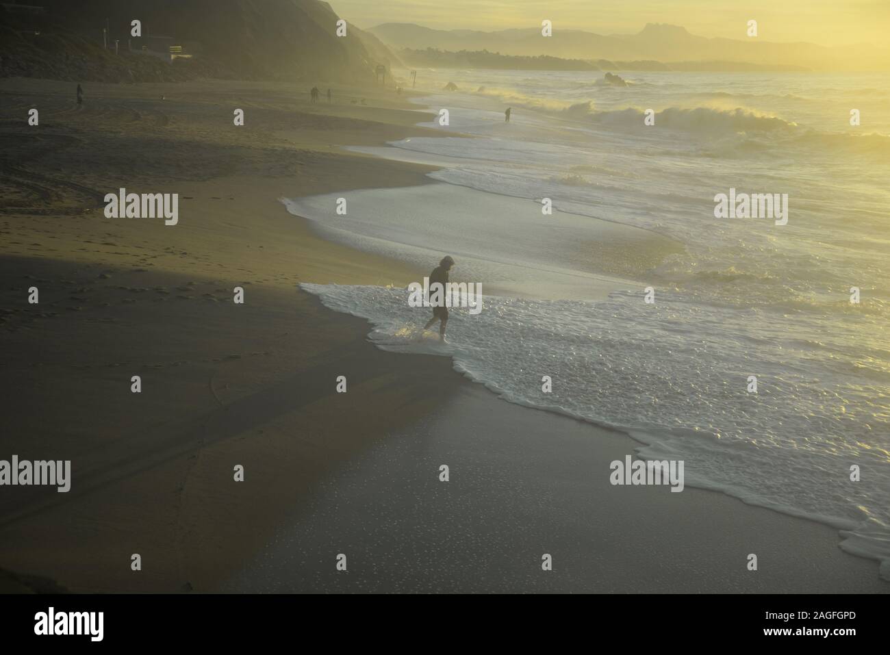 Mann in einem flachen Kappe mit seiner Hose aufgerollt Paddeln in den Wellen des Ozeans, pasakdek Stockfoto
