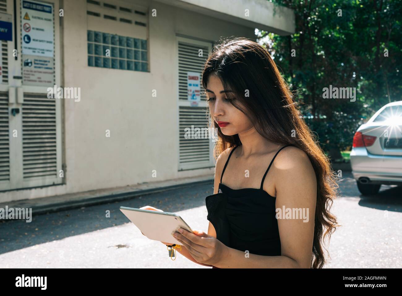 Ein langes Haar Asiatische indische Mädchen halten und über mobile Touchscreen Gerät Tablette outdoor Park Stockfoto