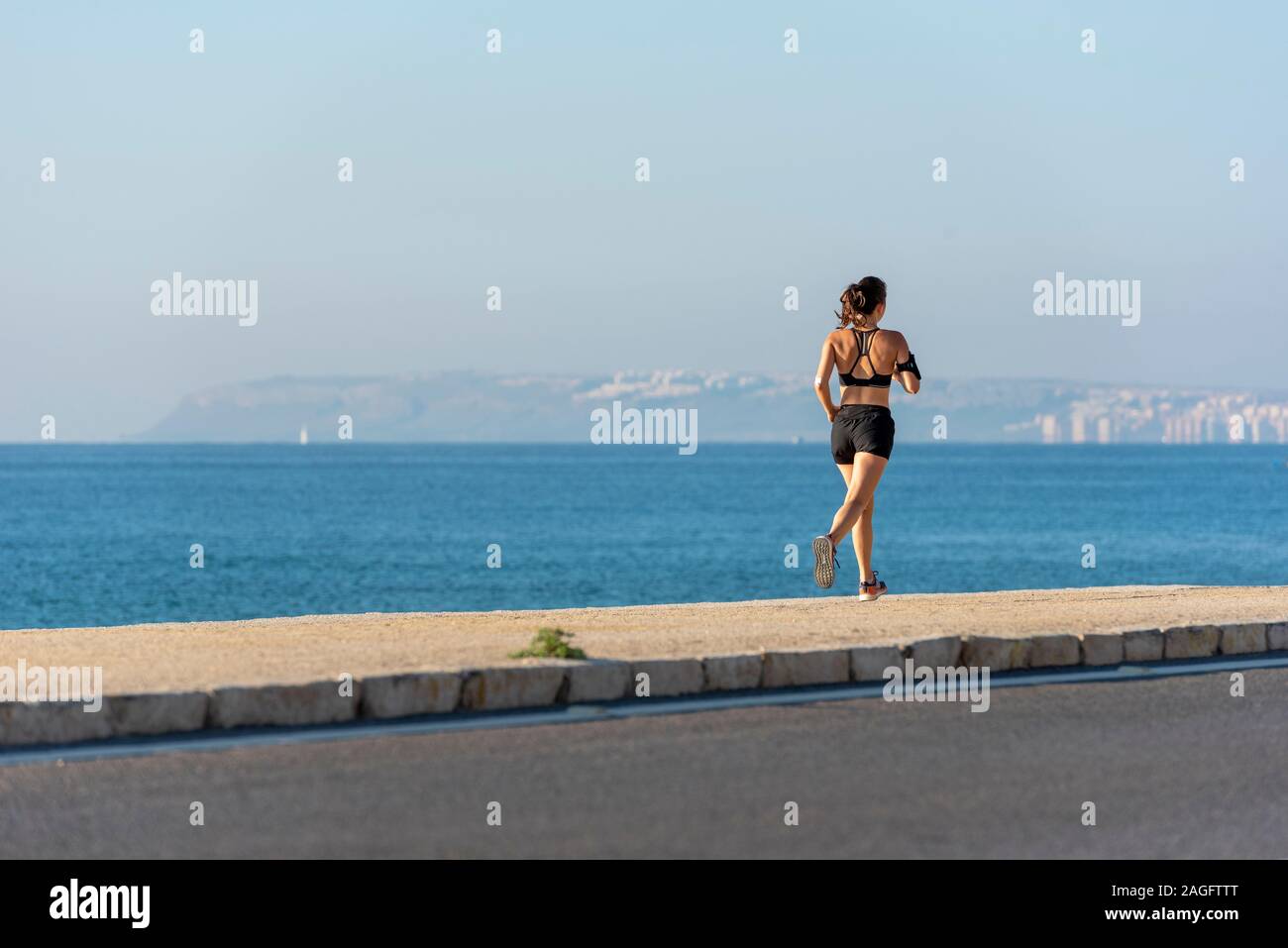 Frau Joggen am Strand mit einem Telefon, Alicante, Spanien. Stockfoto