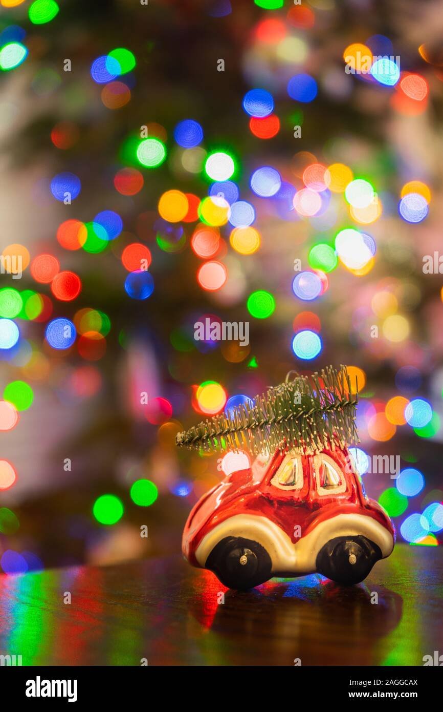 Miniatur rotes Auto ornament Durchführung Weihnachtsbaum auf Holztisch mit bunten Weihnachtslichter Bokeh im Hintergrund Stockfoto