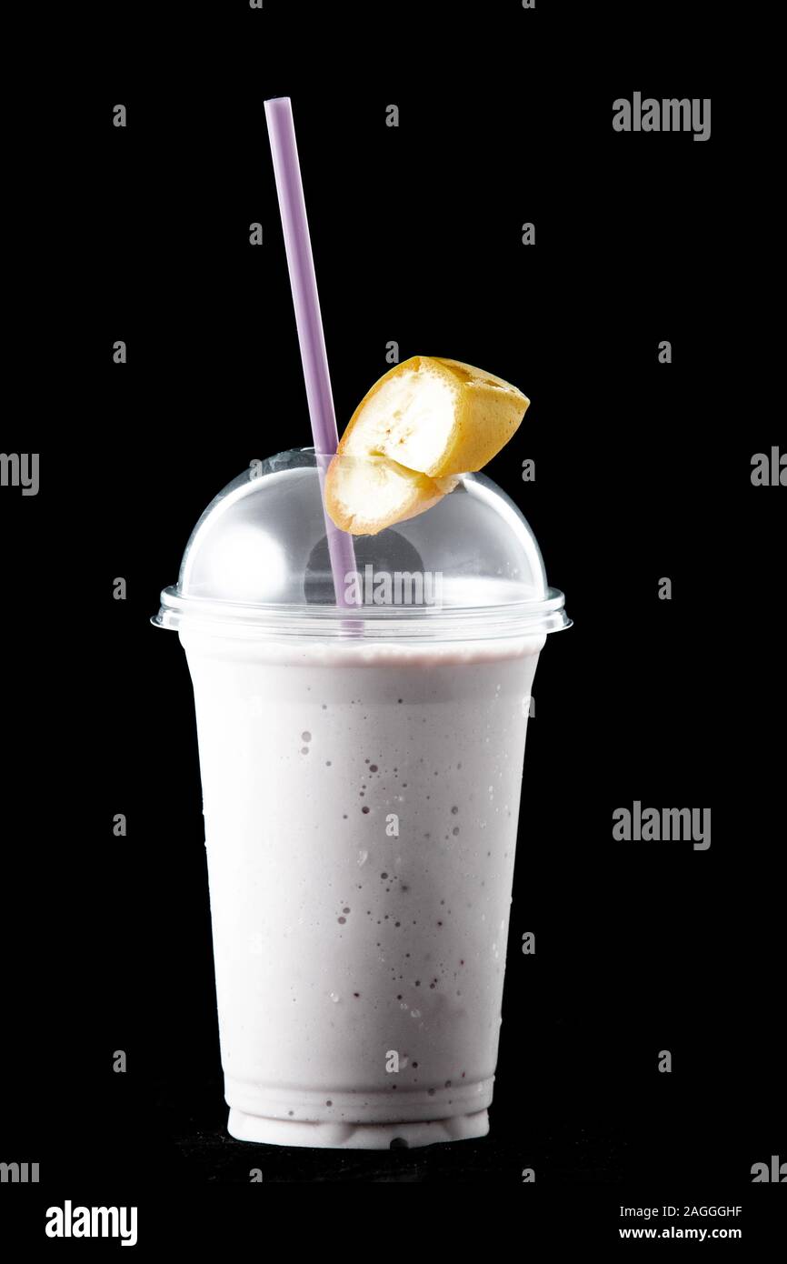 Banane Milchshake in ein Glas und ein Stück Banane auf dem Glas. Es gibt einen Strohhalm in das Glas. Auf schwarzem Hintergrund isoliert. Stockfoto